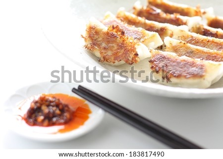 A plate of pot stickers with chopsticks and dipping sauce.