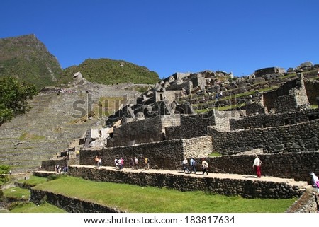 People walk along large stone Incan ruins on a hill, Macchu Pichu, Peru.