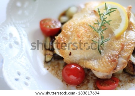 A white bowl of fried chicken, cherry tomatoes with rosemary and lemon dressing.