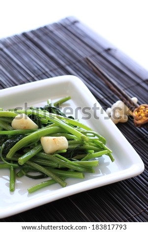 A small white bowl of cooked green vegetables on a woven mat.