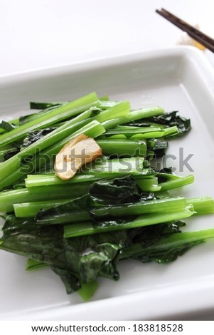 A plate of greens with chop sticks laying on the side.