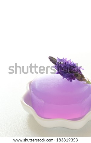 A white soap dish with purple glycerin soap and small purple flowers.