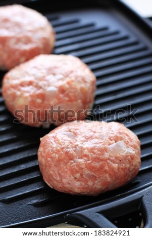 Three uncooked burgers in a pan with grid lines.