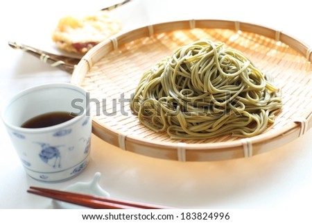 Green noodles on a plate with a cup of tea beside it.