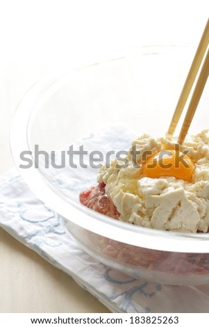 A clear bowl containing an egg yolk, tofu, and ground beef with chopsticks stuck in the top.