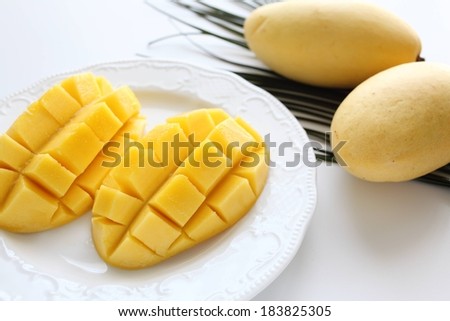 Two diced mangoes in a white dish next to two intact mangoes.