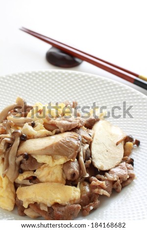 A dish with sliced meat and various mushrooms with brown chopsticks on a side dish.