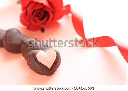 A red rose with a red ribbon and chocolate hearts.