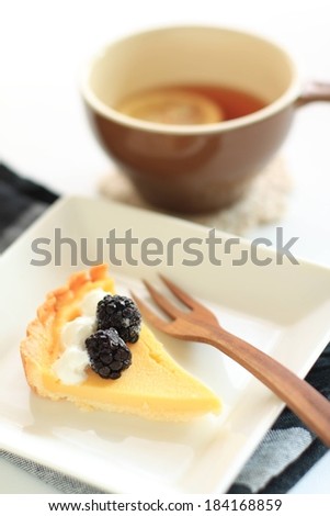 A slice of cheesecake with blackberries and cream served with tea with lemon.