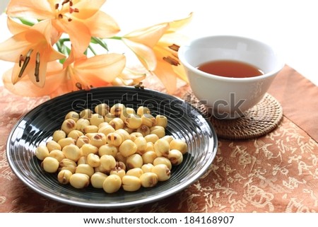Small round food items in a black dish with tea and flowers beside it.