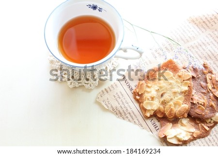 A cup of tea on a lace doily and almond crusted cookies.