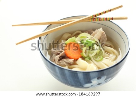 A blue bowl with noodles, carrot, meat and broth and chopsticks placed across the bowl.