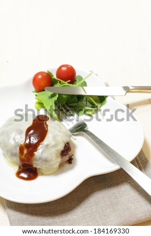Greens and tomatoes with a gravy covered food item on a white plate with cutlery.