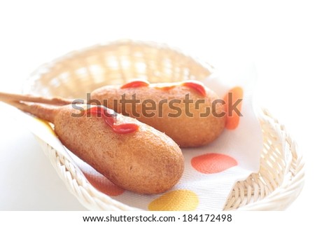 A wicker basket with corn dogs topped with ketchup.