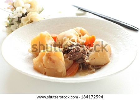 A dish of meat and vegetables with flowers behind as a decoration.