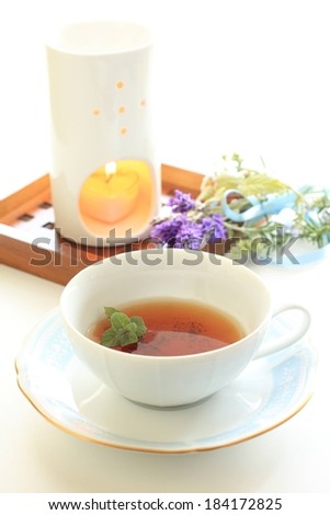 A lit candle on a wooden box with flowers and a cup of tea.