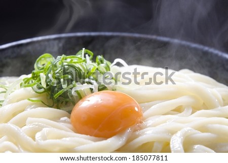 A yolk sits on top of a pile of steaming noodles.