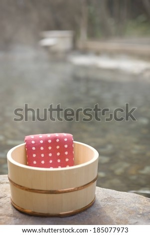 A red towel with white dots is lying over the edge of a wooden bucket.