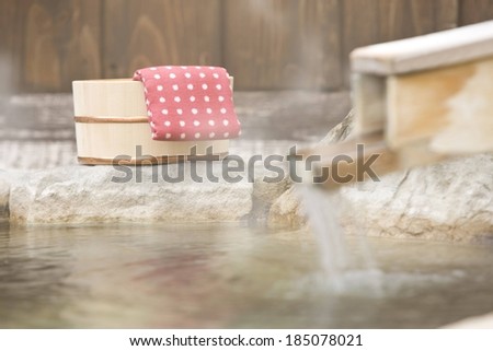 A steaming hot spring with flowing water, bucket and a towel.