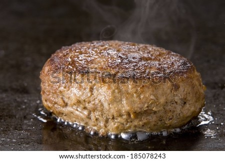 A beef burger patty cooking on a grill.
