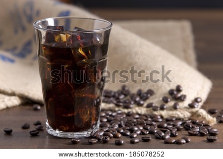 A glass of black iced coffee surrounded by coffee beans.