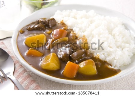 A meal of white rice and stew on a white plate with a spoon and fork.