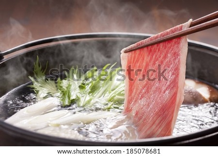 A steaming pot of red meat and raw vegetables.