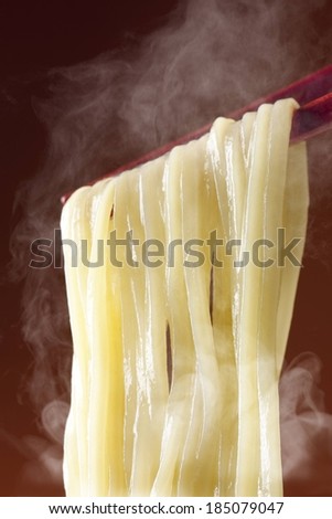 Steamy lo mein noodles being held with chopsticks.