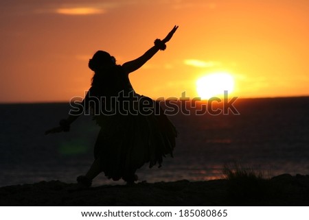 A hula dancer silhouetted against the sunset as she dances.