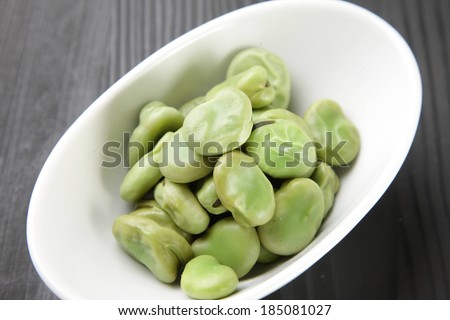 A white bowl on a wooden table with lima beans in it.