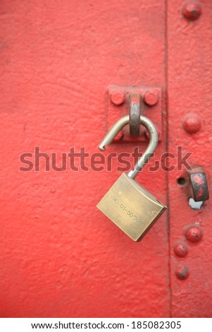 An unlocked padlock hanging through a steel loop on a metal door.
