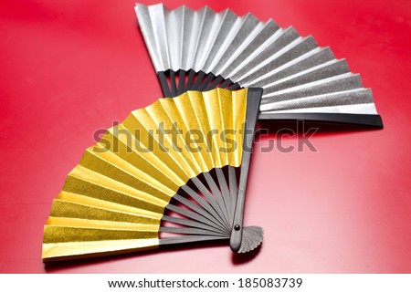 Two different colored fans made of paper lying on a red table.