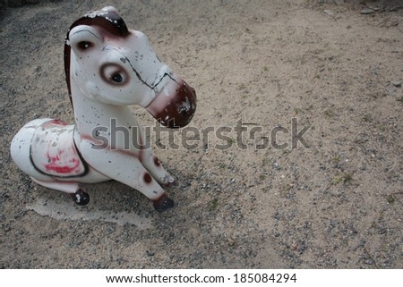 A sad and broken toy horse sitting on a concrete block surrounded with pebbles.
