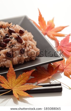 A plate with rice and beans beside leaves and chopsticks.