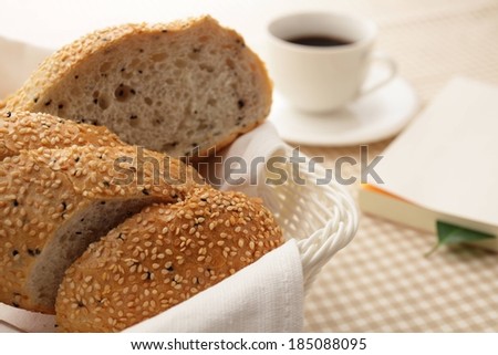 A cloth lined wicker basket of bread beside a cup and saucer.