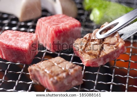 Someone cooking beef on the barbecue and flipping them over.