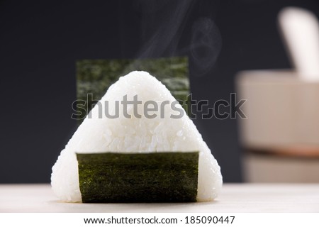 A sushi roll with rice resting on a white surface.