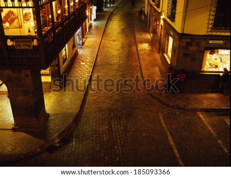 An empty street lined with well-lit stores at night, Cuzco, Peru.
