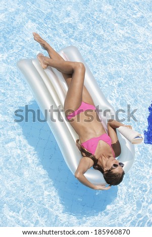 Mid adult woman reading book on pool raft