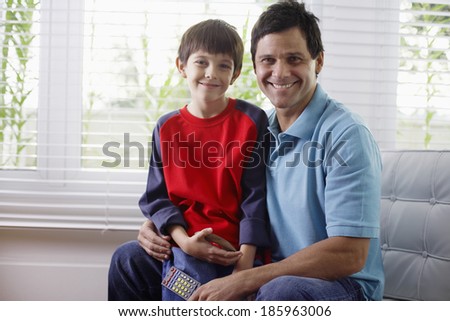Father and son sitting on armchair, father holding remote control