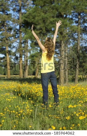 Young woman raising hands in a field of wildflowers