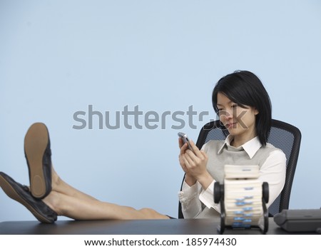 Businesswoman with Feet on Desk Using Cell Phone