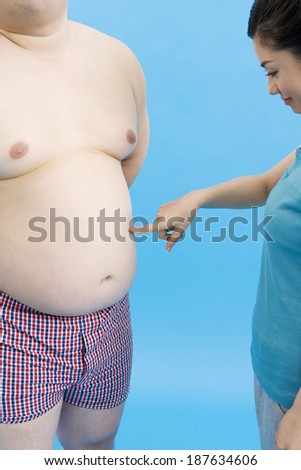 A woman pokes an obese man\'s bare belly.
