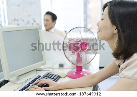 woman using PC on desk with an electric fan