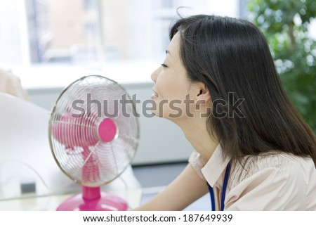 woman sitting at desk with an electric fan