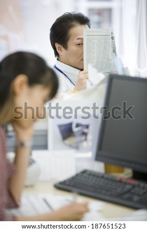 male boss looking at female subordinate and reading newspaper