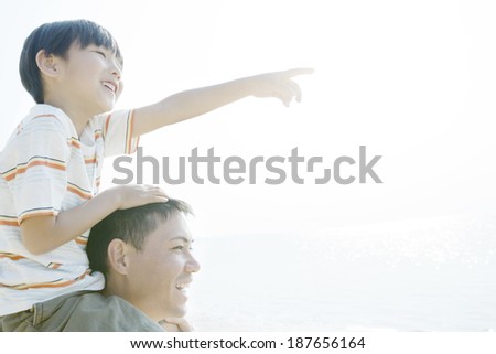 son pointing to the distance on father\'s shoulders