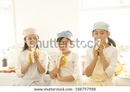 Three Japanese daughters eating banana in kitchen