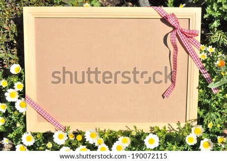 A picture frame, tied with checkered ribbons, propped up in the flowers.