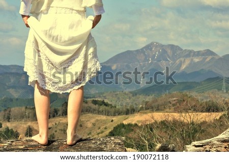Woman wearing lace white skirt looking towards mountains with forest in front. Holding skirt up